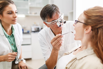 Obraz premium Senior male dentist in dental office talking with female patient and preparing for treatment.