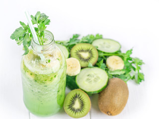 Fototapeta na wymiar Cucumber smoothies in the bottle, kiwi, parsley, and banana on white wooden table.