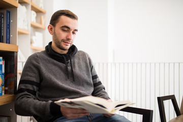 Handsome male student reading a book sitting on the floor in a bookshop