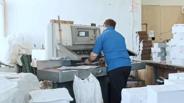Man completes journal pages - manual labour - cutter guillotine machine at printing factory - typography