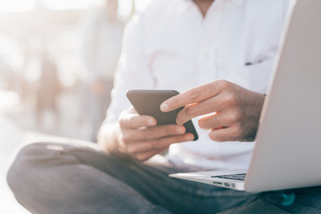 close up hand of young man holding smart phone and using computer - business, social network, multitasking concept