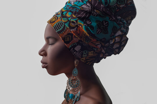 Young beautiful African woman in traditional style with scarf, earrings crying, isolated on gray background. racism, depression or loneliness concept..