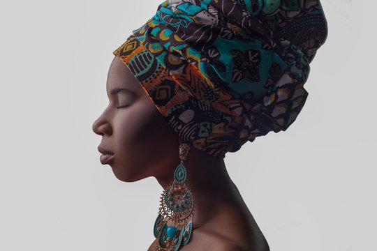 Young beautiful fashion model with traditional african style with scarf, earrings and nude makeup isolated on gray background.
