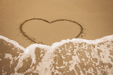 Heart drawn in the sand erased by a wave