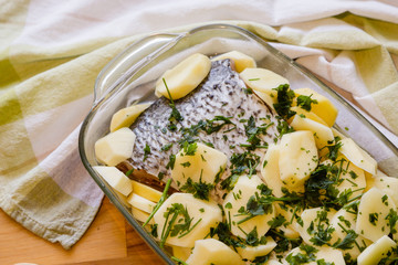Fish filet with potatoe and parsley ready for baking on wooden table background