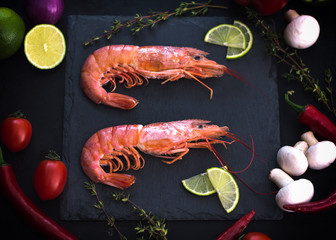 Shrimp on a stone with cherry tomatoes, lime and thyme in a restaurant. Cooking process. Black background. Top view. Close-up