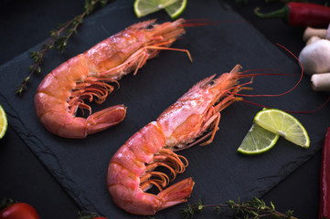 Shrimp on a stone with cherry tomatoes, lime and thyme in a restaurant. Cooking process. Black background. Top view. Close-up