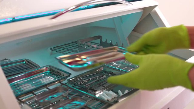 Close up shot of hands in gloves taking instruments from the box for dental instruments disinfection. Ultraviolet sterile chamber. Shot in 4k