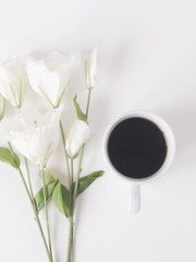 Cup of black coffee with white flowers on white background. Flat lay. Top view