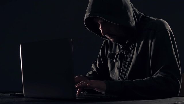 Cyber crime and computer virus concept with hooded faceless person working on laptop