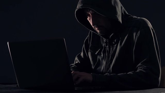 Cyber crime and computer virus concept with hooded faceless person working on laptop