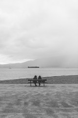 Two people sit on a bench looking out towards English Bay, Vancouver BC.
