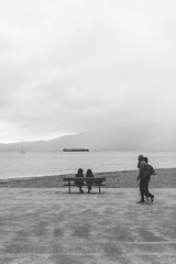 Two people sit on a bench looking out towards English Bay, Vancouver BC.