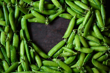 Heart made of fresh green peas on the rustic background. Food frame background.