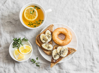 Banana sandwich with chia seeds, donuts and green tea with lemon and thyme on a light background, top view. Delicious breakfast or snack