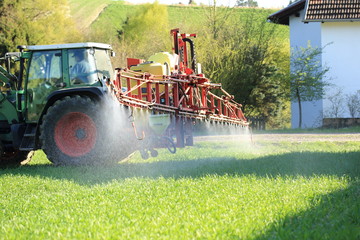 Traktor beim Spritzen von Planzenschutzmittel bei Häusern