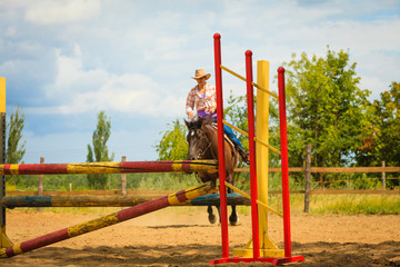 Fototapeta na wymiar Cowgirl in western hat doing horse jumping