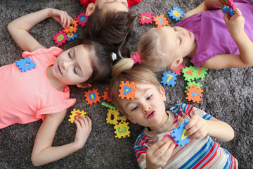Cute little children playing with colorful figures while lying on carpet at home