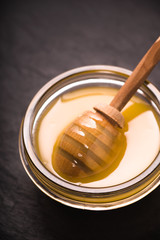 Spoon in a bowl of honey on a dark slate closeup