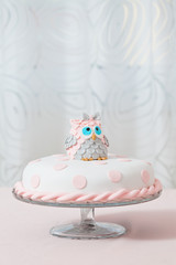 Birthday cake covered with fondant displayed on the pink cloth and glass tray; decorated with pink...