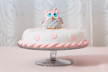 Birthday cake covered with fondant displayed on the pink cloth and glass tray; decorated with pink...