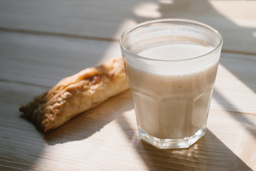 Rustic healthy breakfast with small loaf and yoghurt in a glass on a wooden table. Healthy breakfast with vital vitamins. Sunlight shines through the frame of a window. 