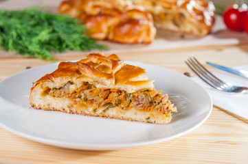 Fresh piece of meat closed pie on the white plate on the wooden served table. Composition of vegetables and ingridients. Close up, selective focus