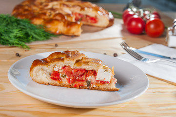 Fresh piece of closed pie with brynza cheese and vegetables on the white plate on the wooden served table. Composition of ingridients. Selective Focus, close up