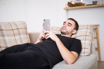 Young smiling man surfing the network and text messaging with mobile phone at home