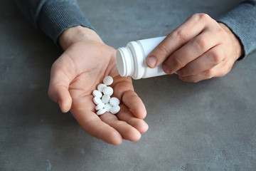 Male hands with pills on grey textured background, closeup
