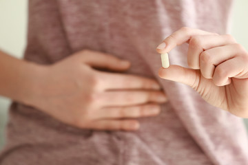 Young woman with pill suffering from pain in belly, closeup