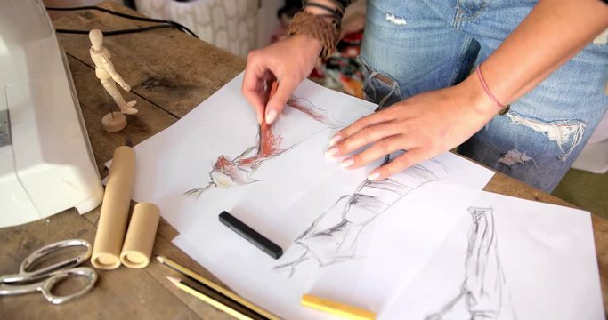 Crop faceless shot of female tailor standing near table in and drawing sketches of dress.