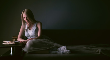 Fototapeta premium Girl enthusiastically reading a book best-selling house under a rug on a comfortable sofa with a lamp