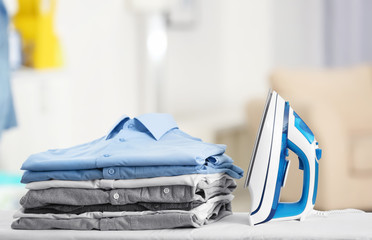 Electric iron and pile of clothes on blurred background