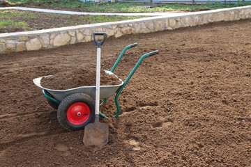 Two-wheeled wheelbarrow loaded with loose soil and a square-point spade on the cultivated area in the autumn garden under reconstruction