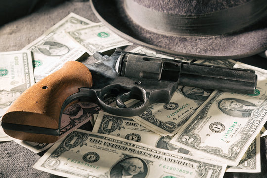 Crime concept. Black gun with dollar banknotes and hat. Toned image