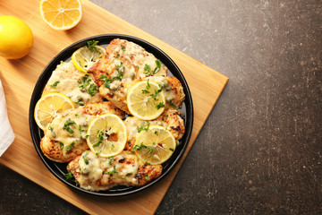 Plate with delicious chicken piccata on wooden board
