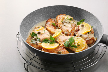 Frying pan with delicious chicken piccata on grey table