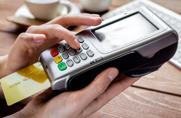 Payment by card in cafe with terminal and keyboard on wooden background