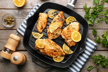 Frying pan with tasty Italian chicken piccata on table