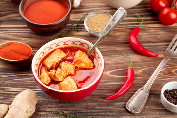 Portion of chicken tikka masala with different spices on wooden table