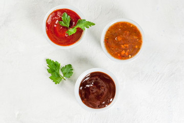 Three kinds of red tomato sauce on a white stone table: traditional classic ketchup, barbecue sauce, sweet and sour Chinese sauce. Top view copy space