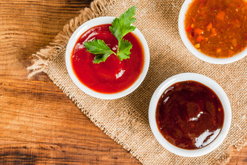 Three kinds of red tomato sauce on a wooden cutting board: traditional classic ketchup, barbecue sauce, sweet and sour Chinese sauce. Top view copy space