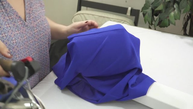 Woman's hands ironing the blue dress closeup