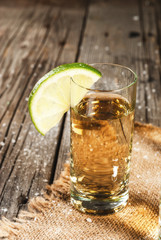 Traditional Mexican alcoholic beverage is a golden tequila. In tall glasses, with a slice of lime and salt on the background. On a wooden rustic table. Copy space