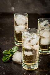 Alcohol cocktail made from golden tequila with ice cubes and mint. On a black concrete table. Copy space