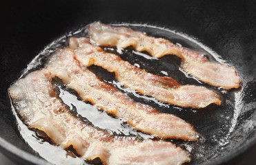 Strips of bacon cooking on pan, closeup