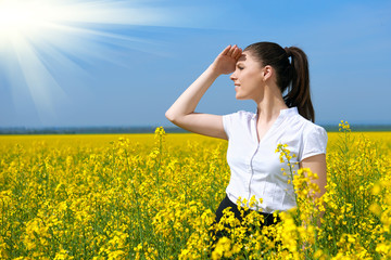 Naklejka na ściany i meble Business woman looking into the distance. Young girl in yellow flower field. Beautiful spring landscape, bright sunny day, rapeseed