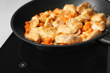 Chicken stir fry with vegetables in pan on electric stove, closeup