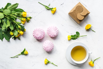 woman desk with marsh-mallow and flowers on white marble background top view